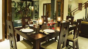 A dining area with a dark wooden table, six chairs, candles, and a ceiling fan. - The Oasis Retreat Seminyak (Seminyak)