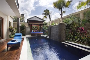 A swimming pool with a wooden deck and lounge chairs, surrounded by tropical plants and a small gazebo. - The Oasis Retreat Seminyak (Seminyak)