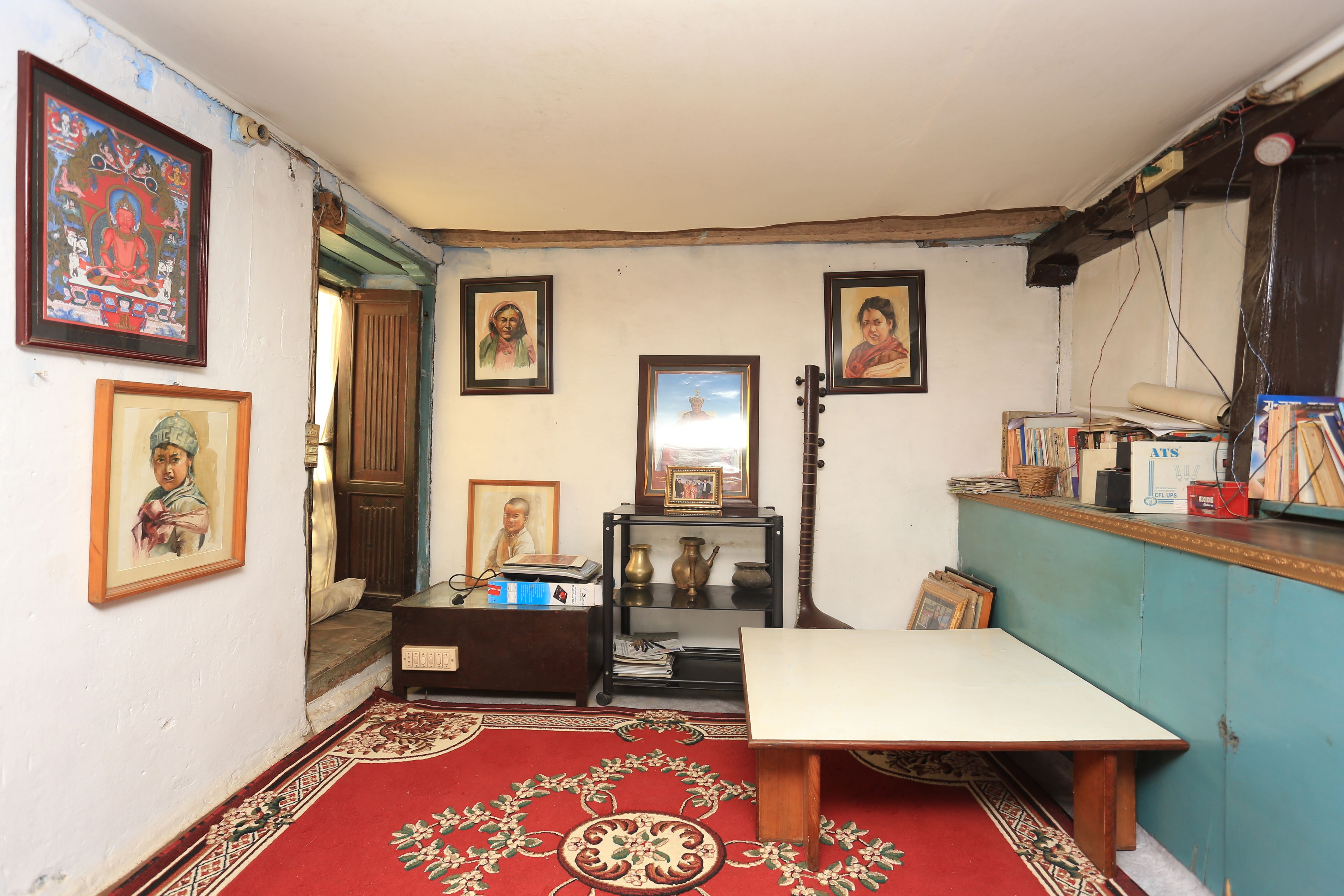 Una habitación con una alfombra roja estampada, una mesa de madera y varias fotos enmarcadas en las paredes.