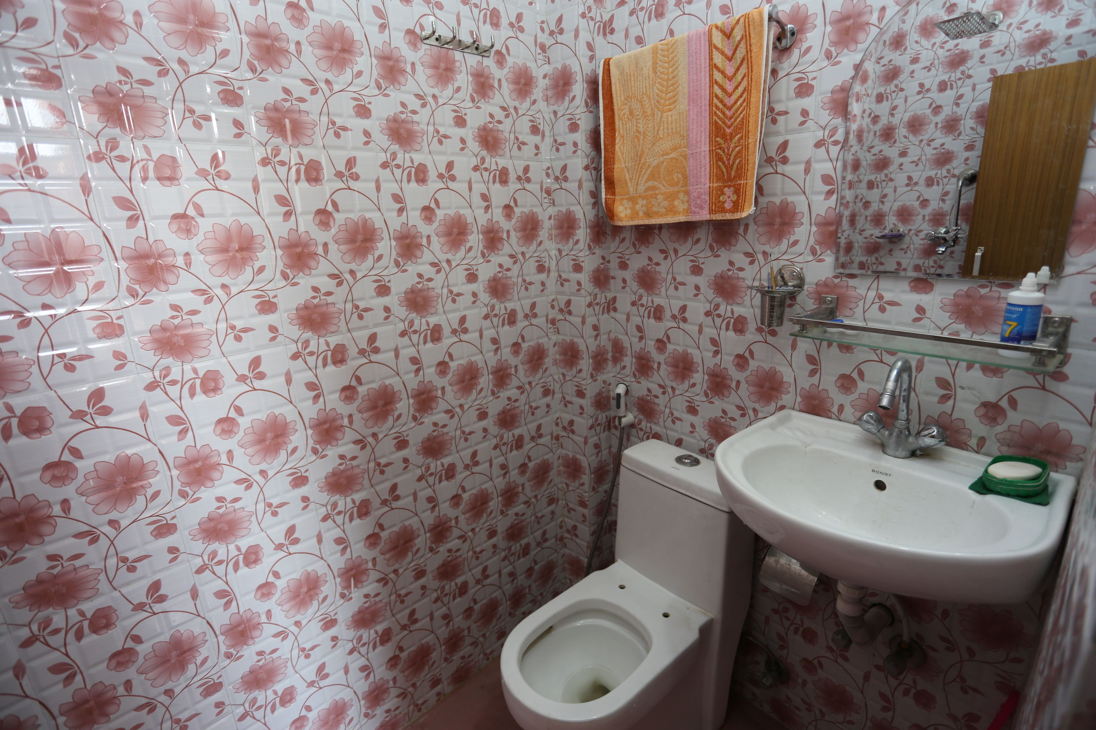A bathroom with floral wallpaper, a toilet, a sink, and a shower.