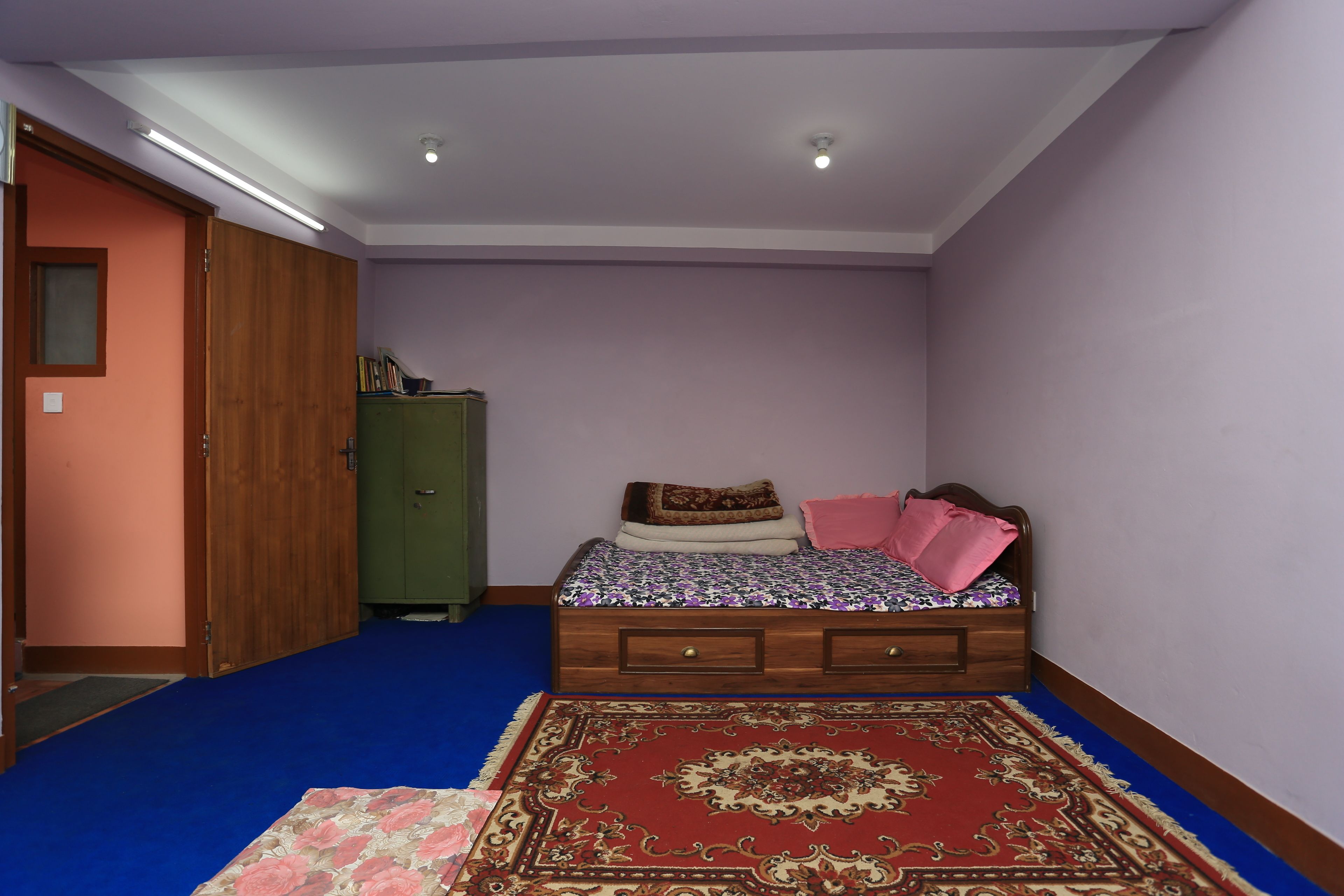 A bedroom with a bed, a wardrobe, a green cabinet, and a red carpet.