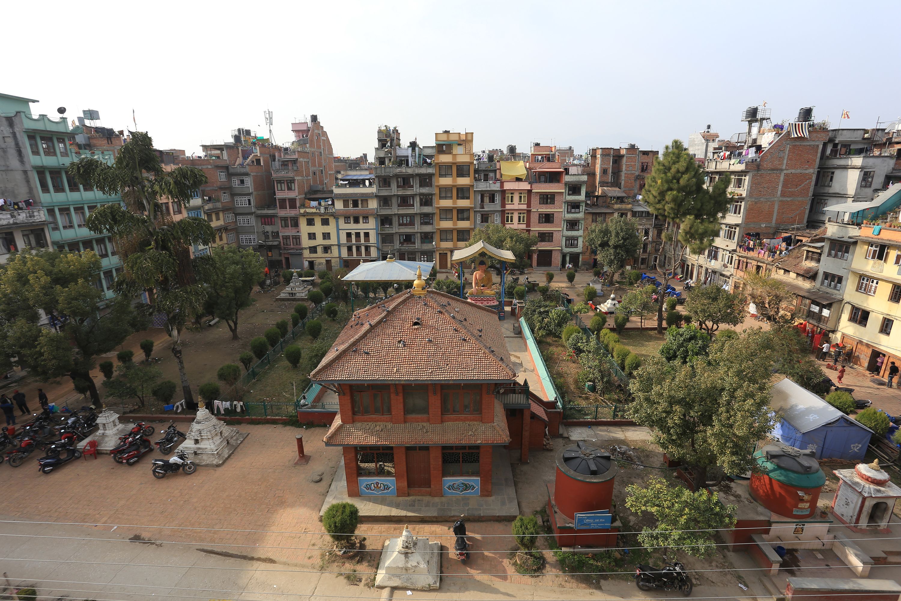A multi-story building with a tiled roof, surrounded by trees and parked motorcycles.