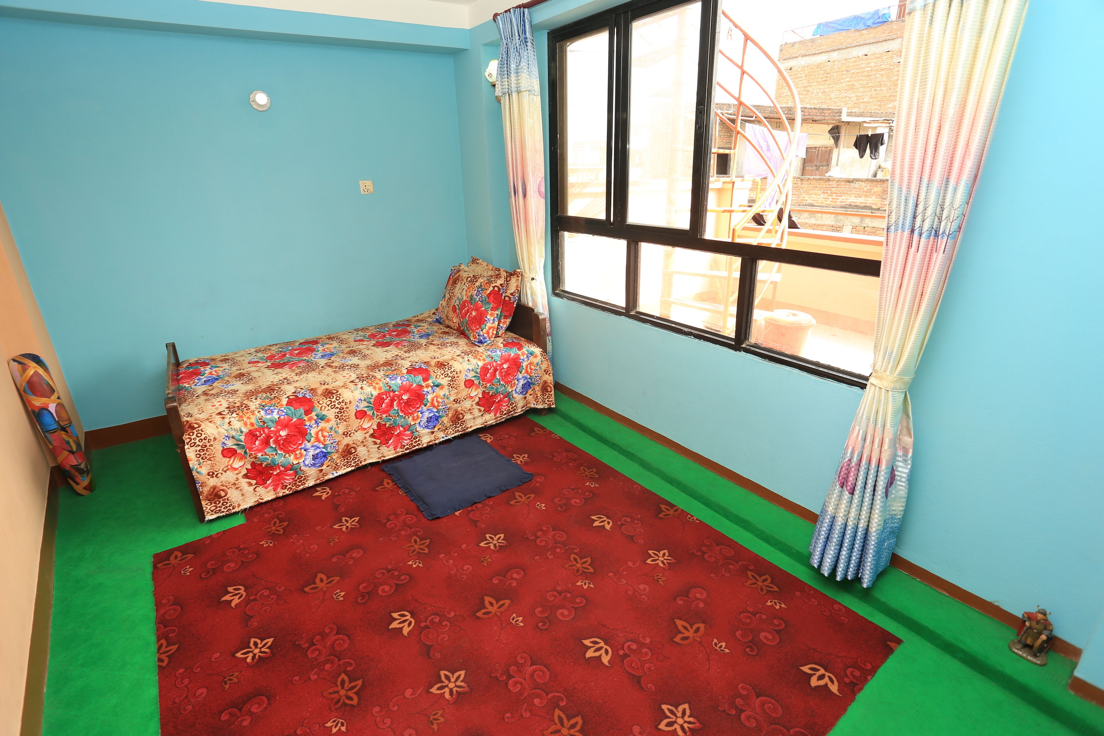 Une petite pièce avec un lit simple, une fenêtre avec des rideaux, une moquette verte et une petite table.