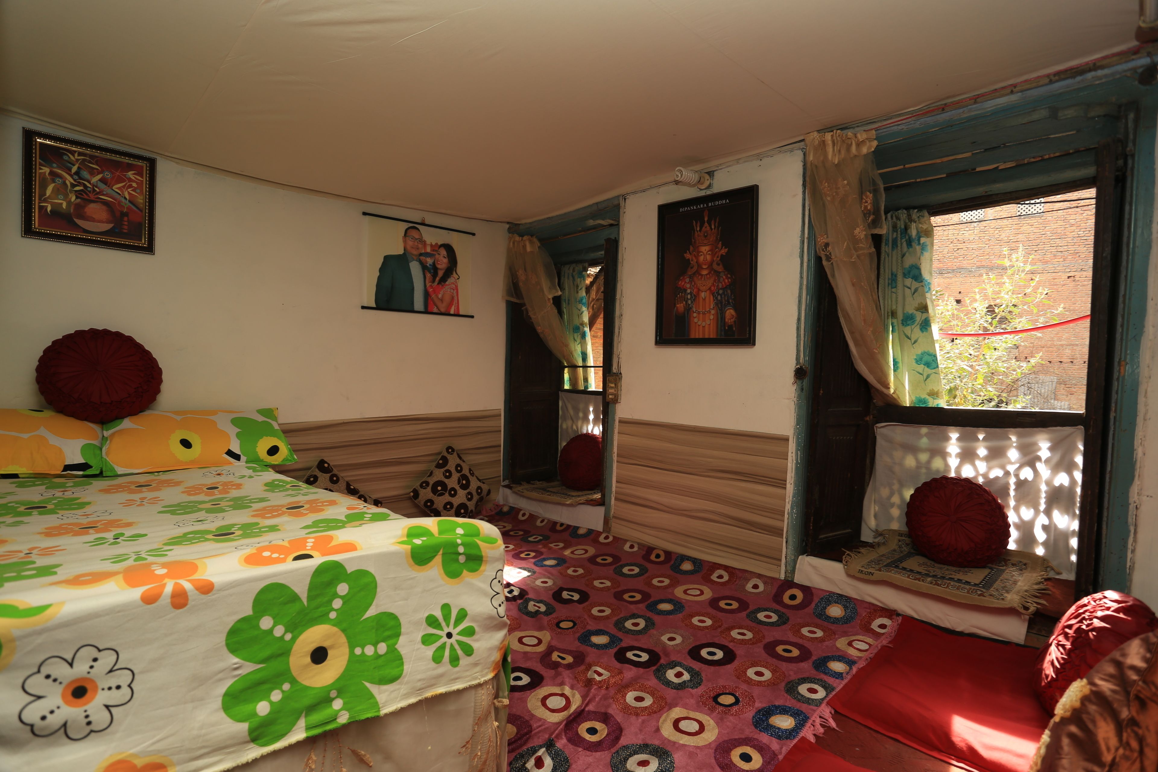 A bedroom with a bed, a window with curtains, a wall with a framed picture, and a patterned carpet.