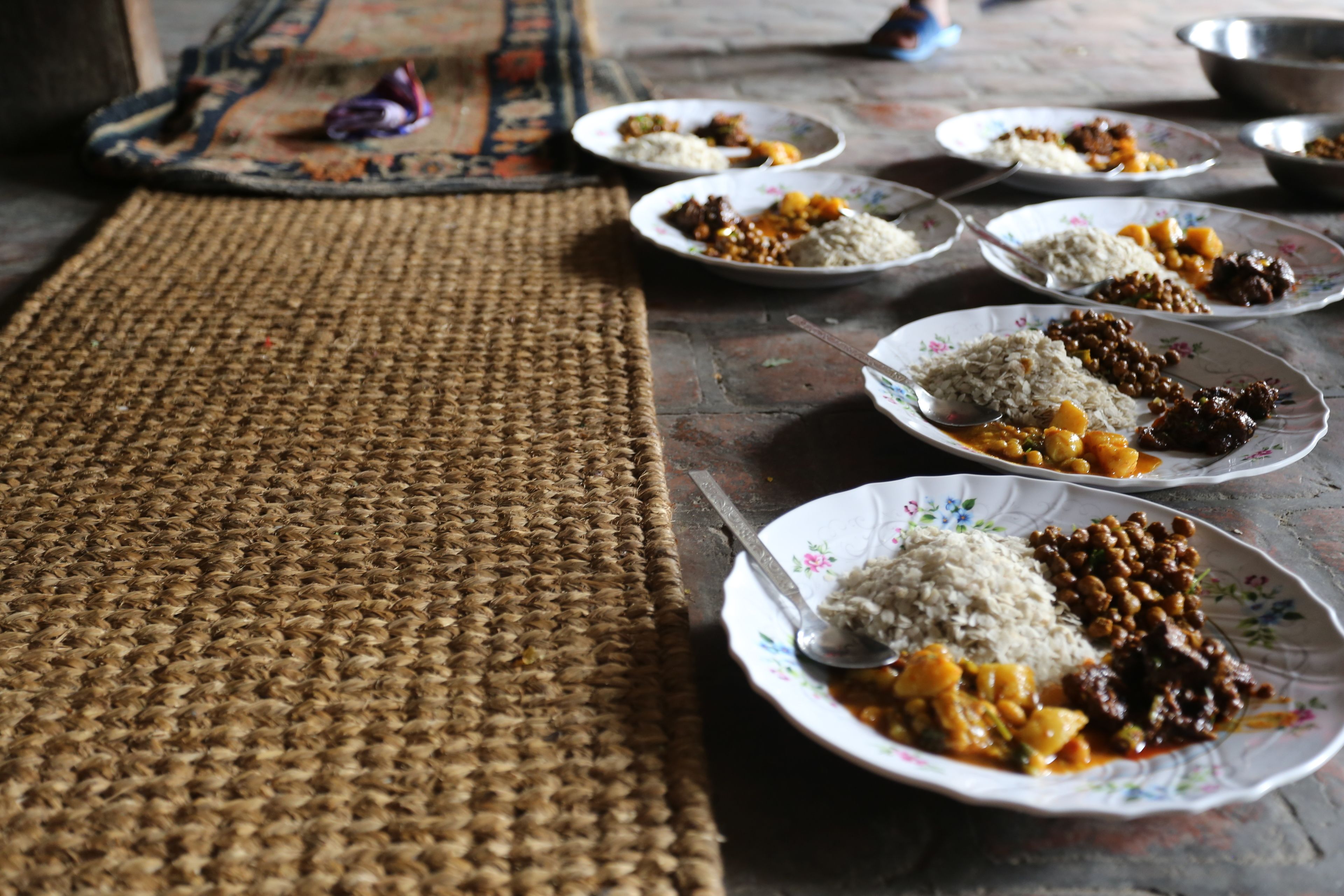 A table with plates of food, a woven mat, and a metal bowl.