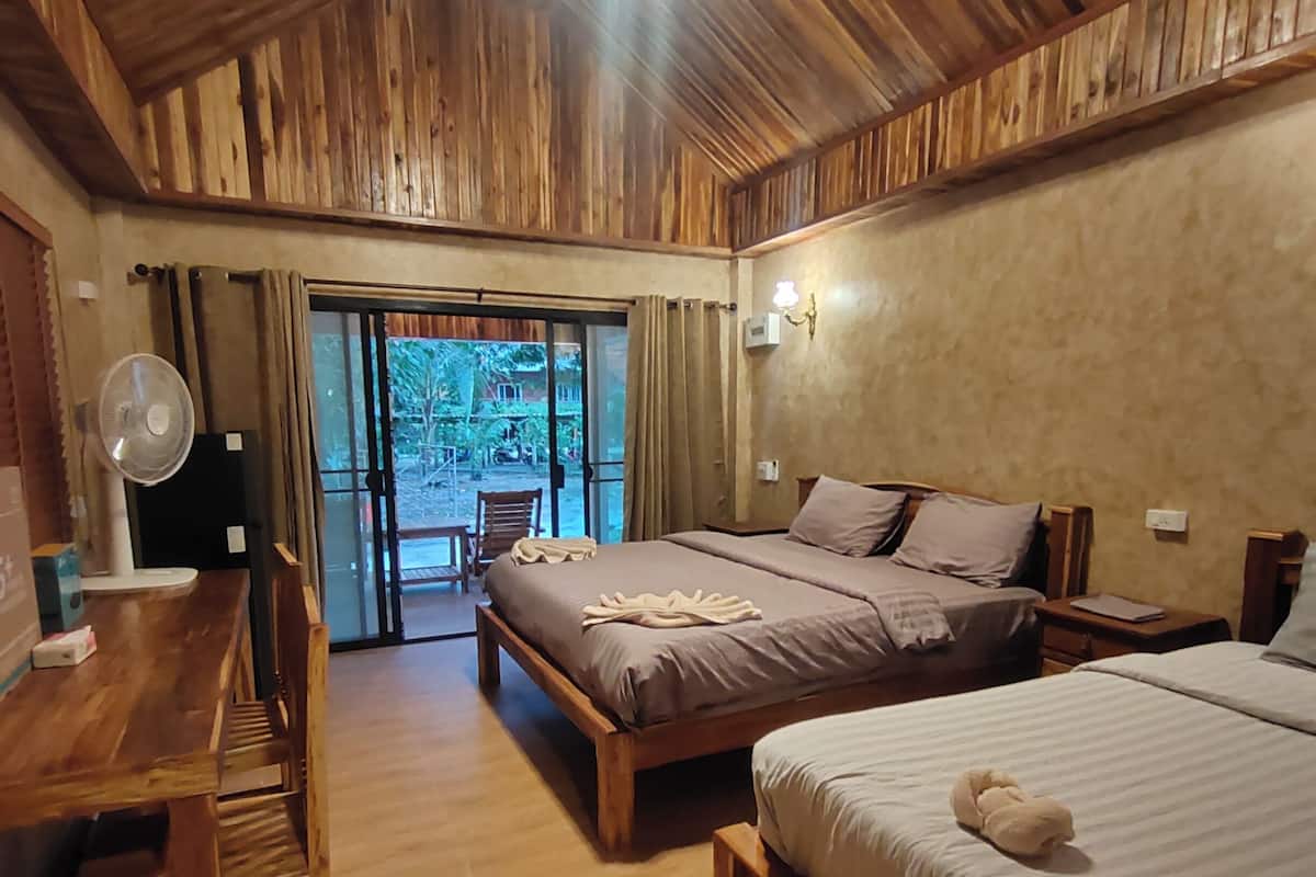 A wooden-floored room with two beds, a desk, and a fan.