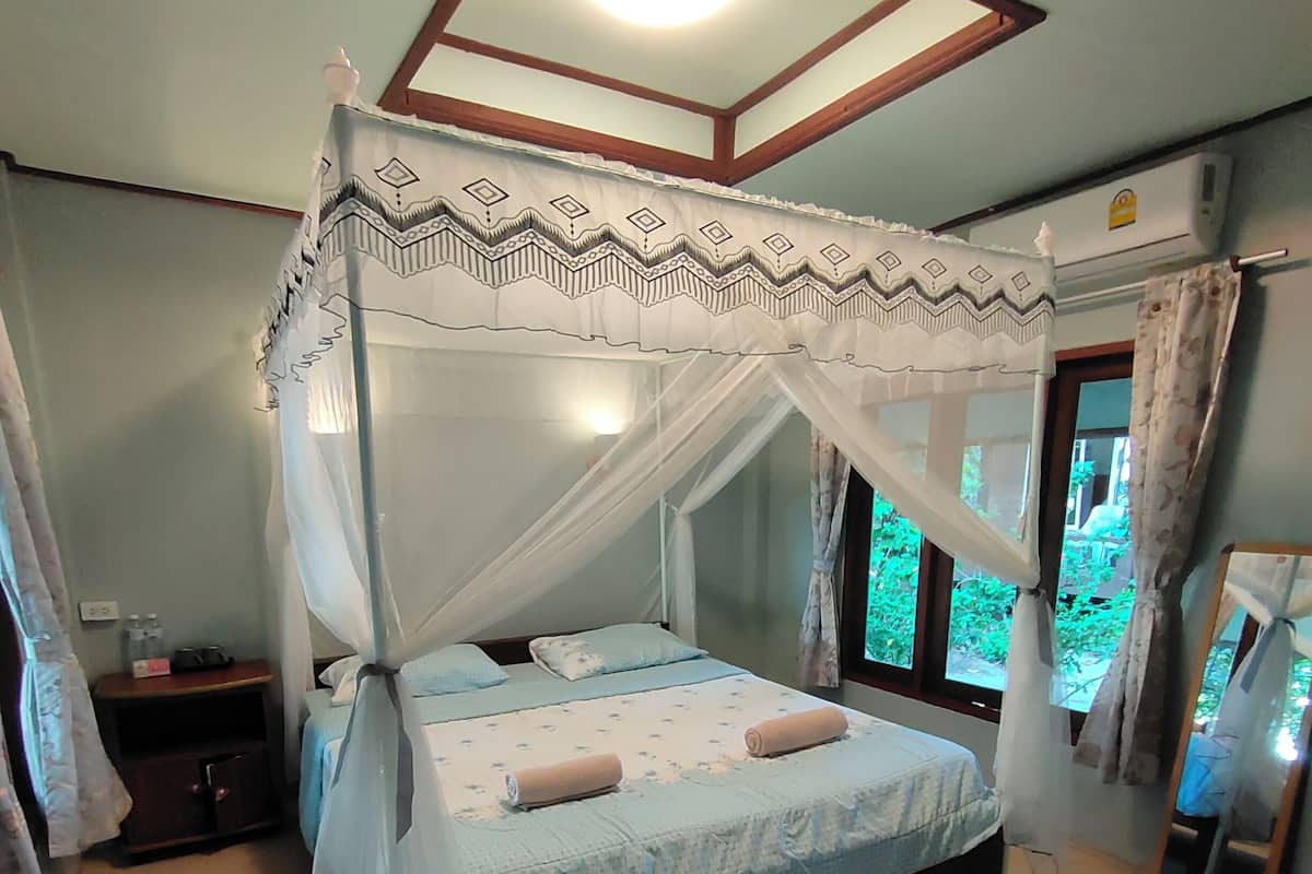 A bedroom with a four-poster bed, a nightstand, and a window with curtains.