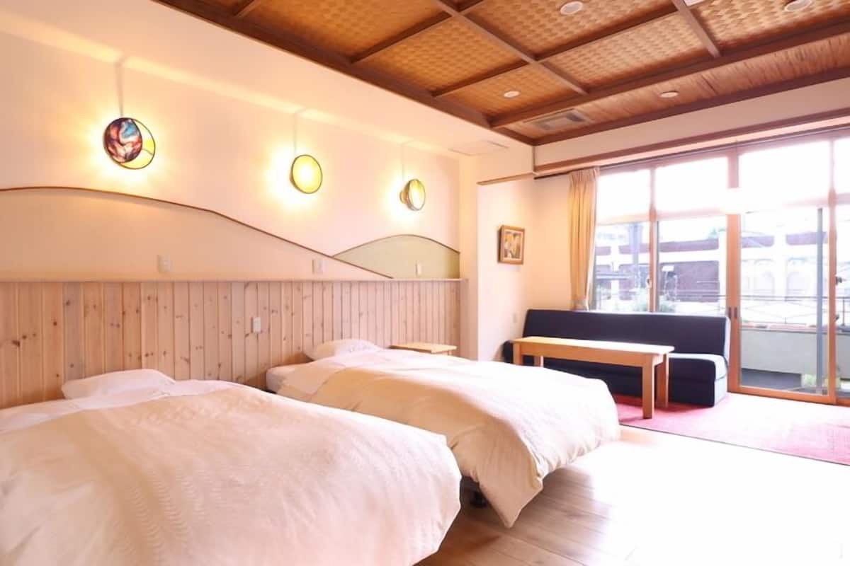Une chambre d’hôtel avec deux lits, une tête de lit en bois, un banc, une grande fenêtre et une vue sur l’extérieur.