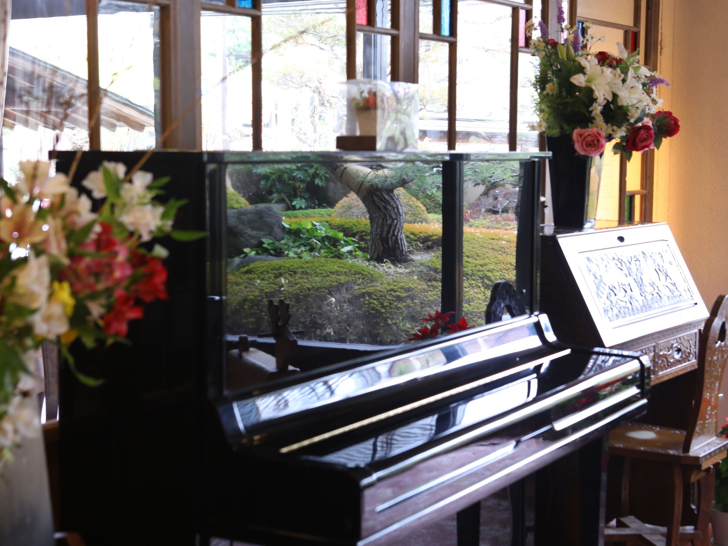 A piano with a view of a garden through a window.