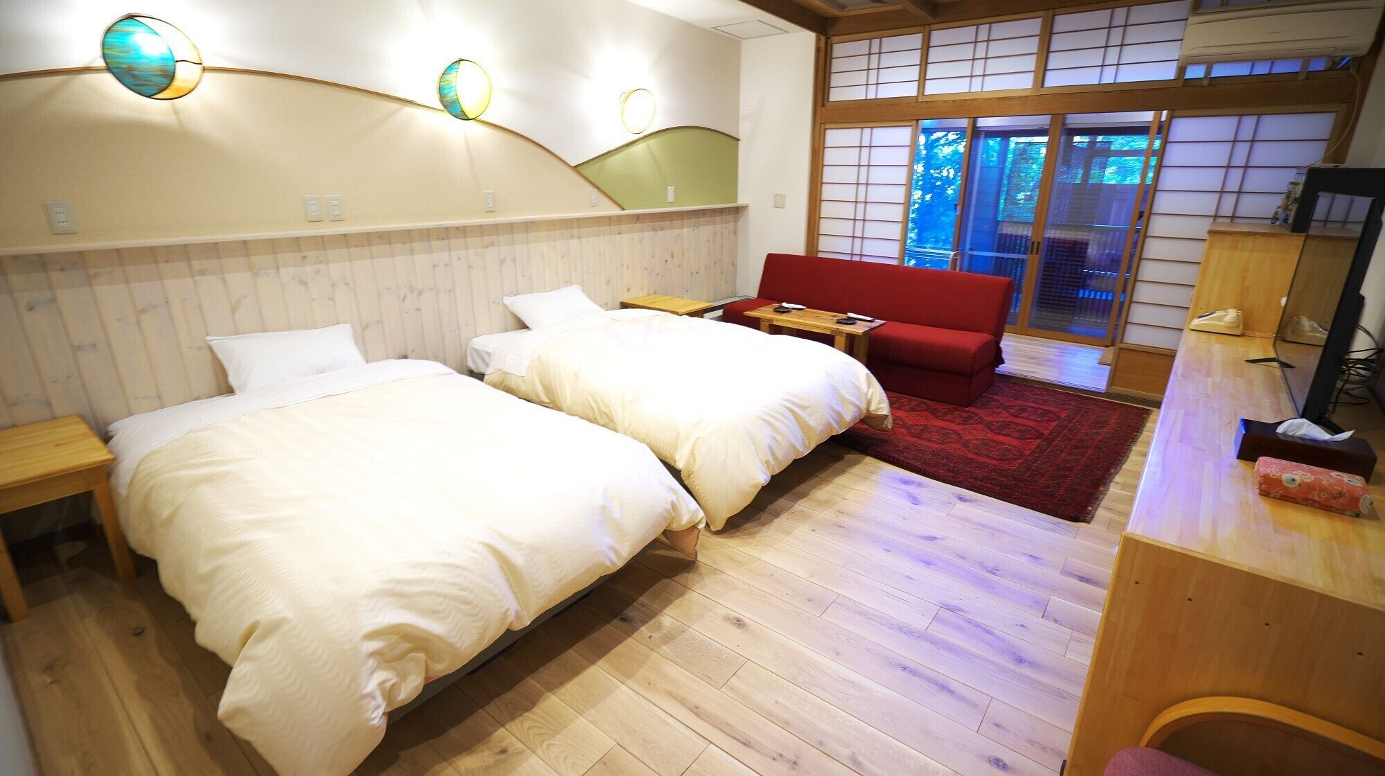 A hotel room with two beds, a red sofa, a wooden desk, and a traditional Japanese sliding door.