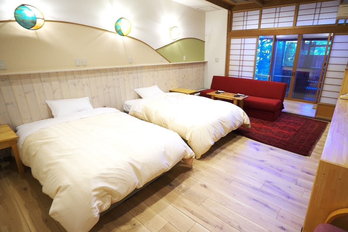 Hotellihuone, jossa on kaksi sänkyä, punainen sohva, puinen työpöytä ja perinteinen japanilainen liukuovi.