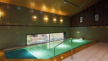 A swimming pool with a wooden deck, a glass wall, and a tiled floor.