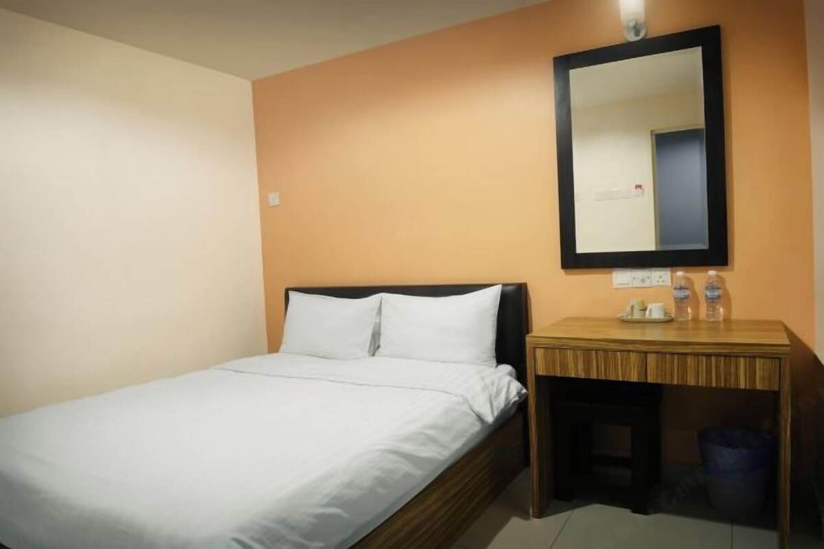 A hotel room with a single bed, a wooden nightstand, a mirror, and a small desk with a trash bin.