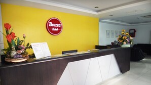 A hotel reception desk with a Brezza Hotel sign, a menu, and a flower arrangement. - Brezza Hotel (Lumut)