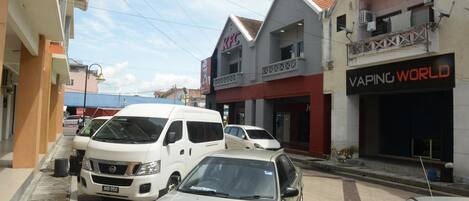 A street with parked cars, a KFC restaurant, and a building with a sign reading "Vaping World".
