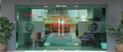 Entrada de hotel con un felpudo de 'Bienvenido', puertas de cristal y plantas en macetas.