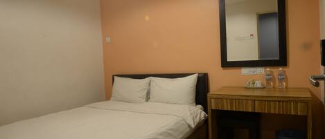 A hotel room with a bed, a wooden nightstand, a mirror, and a trash bin.
