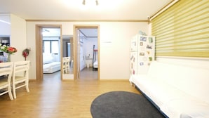 A modern living room with a white sofa, a dining table with chairs, a black rug, and a ceiling light fixture. - Liz's House - Hostel (Seoul)