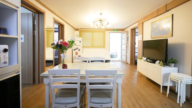 A modern kitchen with a dining area, wooden cabinets, a refrigerator, and a television. - Liz's House - Hostel (Seoul)