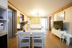 A modern kitchen with a dining area, wooden cabinets, a refrigerator, and a television. - Liz's House - Hostel (Seoul)