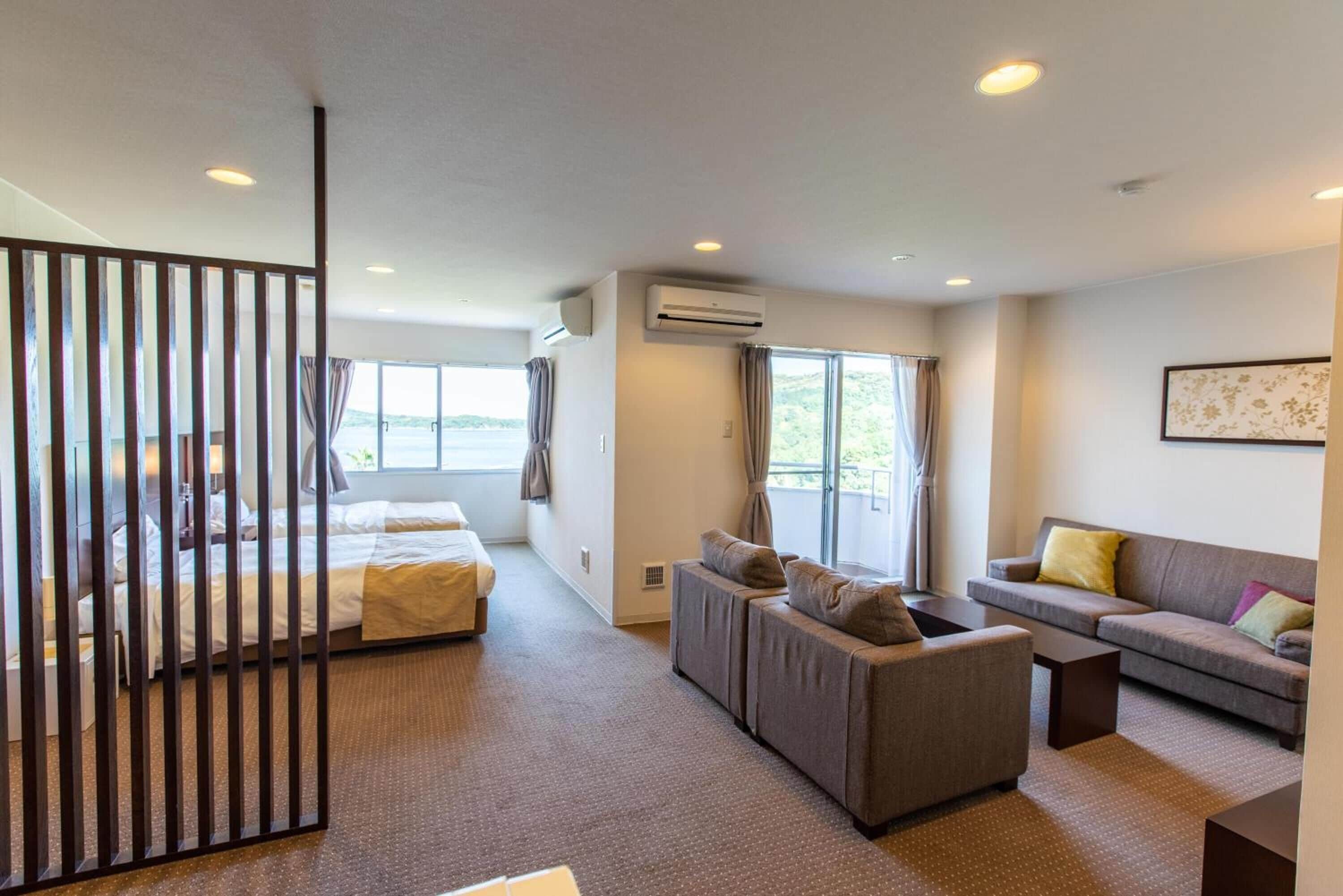 Una habitación de hotel moderna con cama, sofá, una mesita y un amplio ventanal con vistas al exterior.