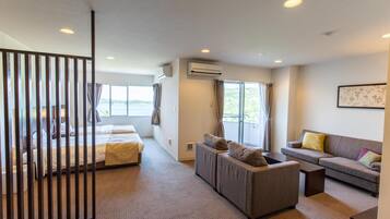 A modern hotel room with a bed, a sofa, a small table, and a large window offering a view of the outdoors.