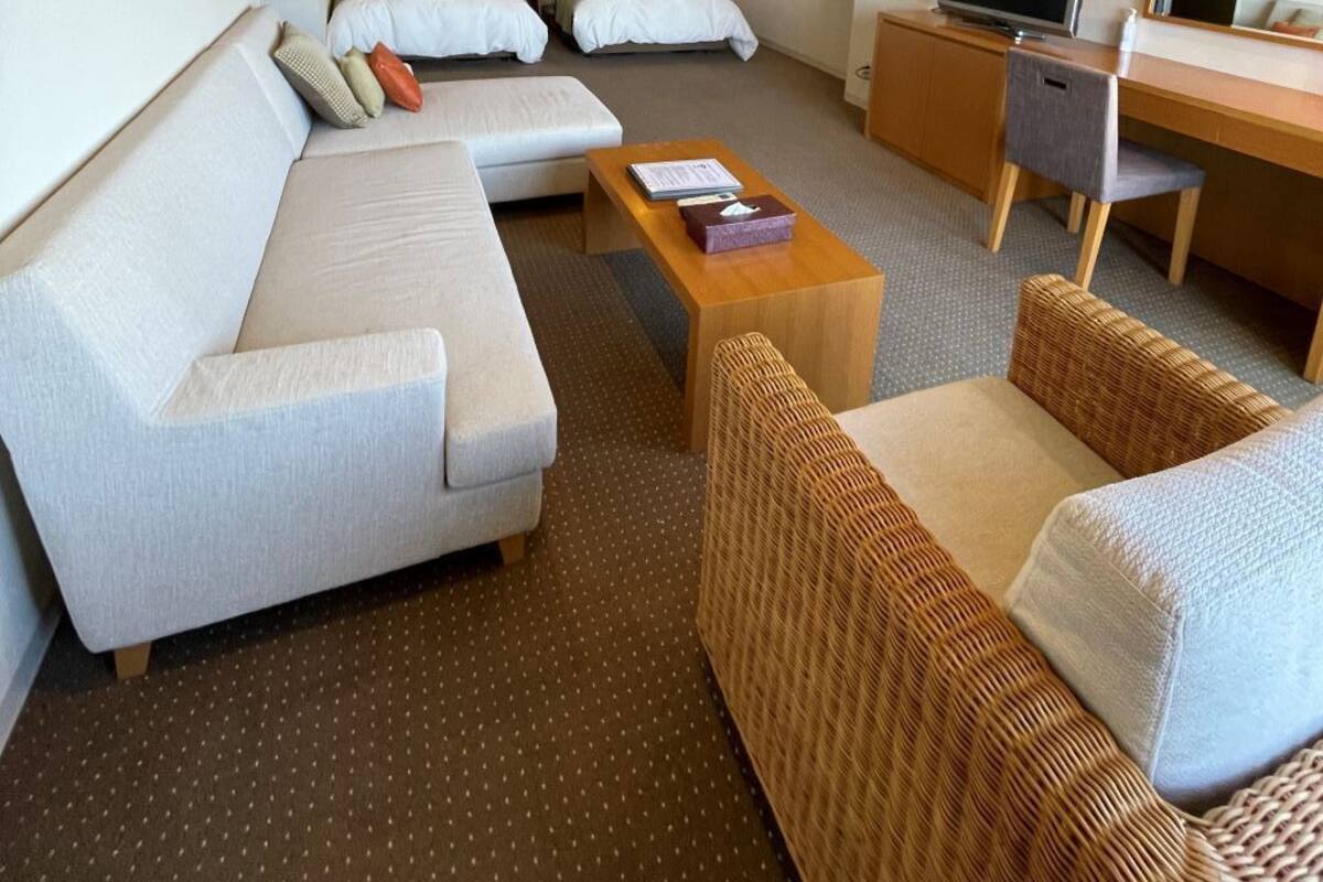 Een hotelkamer met een bank, twee bedden, een televisie, een bureau en een rieten stoel.