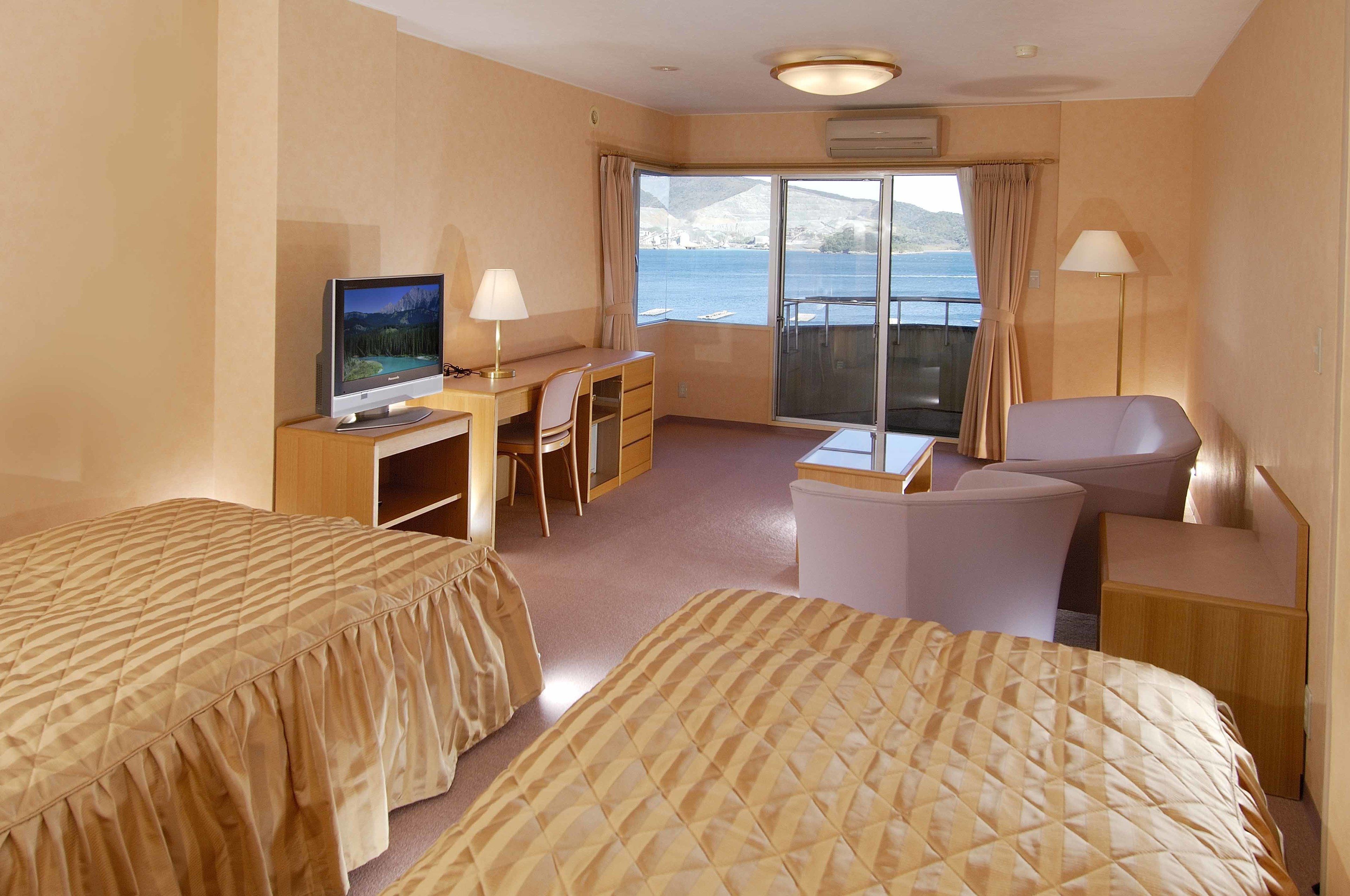 Habitación de hotel con dos camas, un escritorio con computadora, una silla, un sofá y vista al mar.