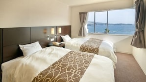 A hotel room with two beds, a large window with a view of the sea, and a headboard with a light fixture.