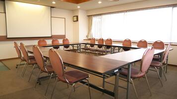 A conference room with a long table and chairs, a projector screen, and a clock on the wall.