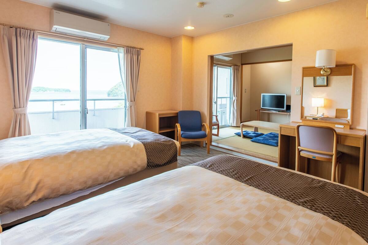 Hotelkamer met twee bedden, een bureau, een stoel, een televisie en een raam met gordijnen.