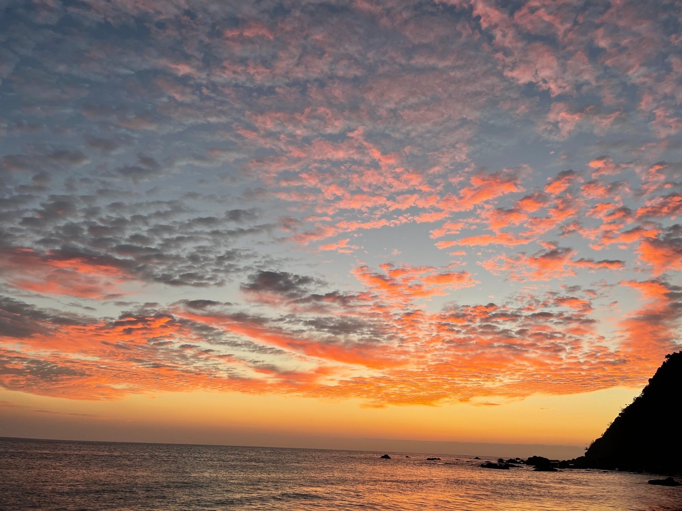 Un coucher de soleil sur l’océan, avec une côte rocheuse.
