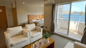 A hotel room with a balcony, a bed, two white sofas, a wooden coffee table, and a view of the sea.