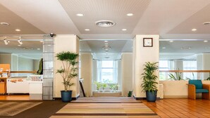 A spacious lobby with a central staircase, potted plants, and a reception desk.