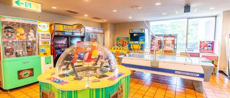 A brightly lit arcade with various gaming machines, including claw machines and racing games.