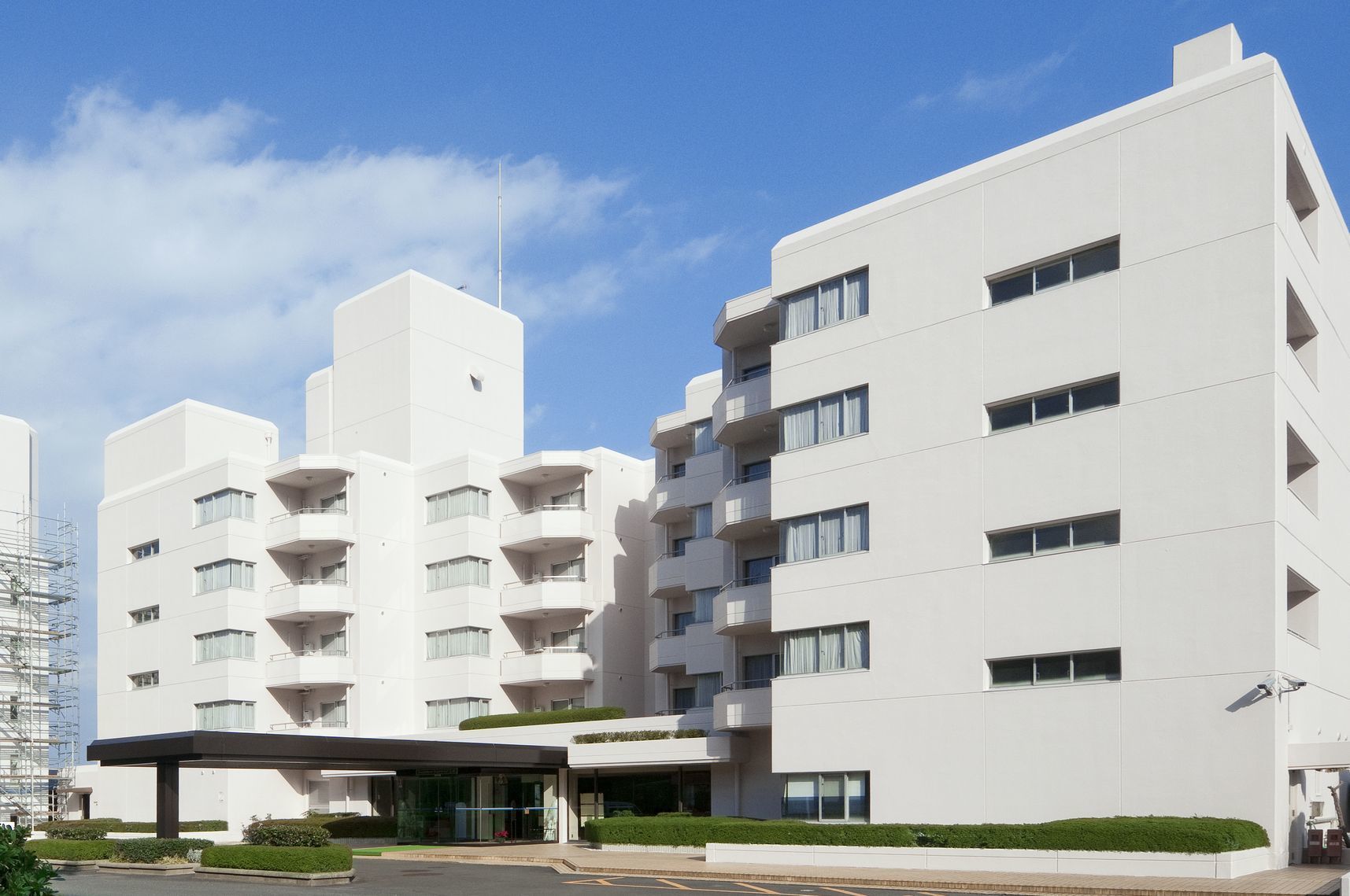 Un hotel moderno de varios pisos con fachada plana, balcones y una zona de entrada cubierta.