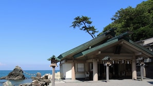 A traditional Japanese building with a green roof, located near a rocky coastline.