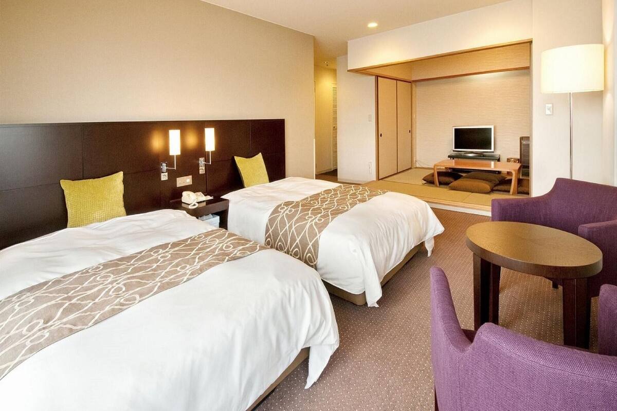 Een hotelkamer met twee bedden, een televisie, een bank en een klein tafeltje.