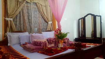 A neatly made bed with multiple pillows and a decorative blanket. A vase with flowers is placed on the bed.