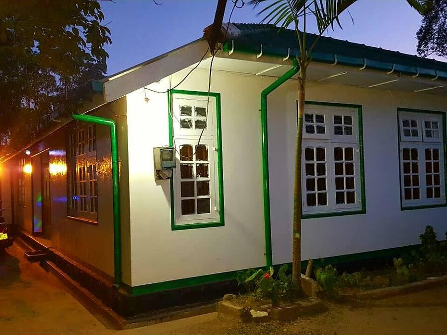 A small, single-story building with a white exterior and green trim. It has multiple windows with white frames and a door.