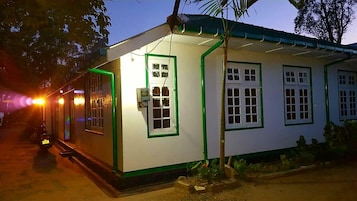 Un edificio pequeño de una sola planta con fachada blanca y detalles en verde. Cuenta con varias ventanas de marco blanco y una puerta.