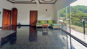 Um hall de hotel com piso de mármore, portas de madeira, um sofá verde e uma grande janela com vista para árvores.