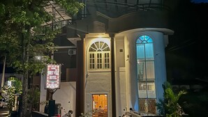 Entrada de hotel com varanda coberta, placa de identificação e um carro estacionado.