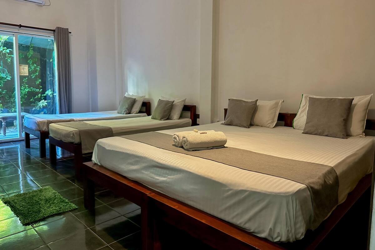 A hotel room with two beds, a large window, and a green mat on the floor.