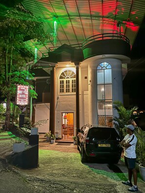 A hotel entrance with a signboard, a vehicle parked in front, and a person standing near the entrance.