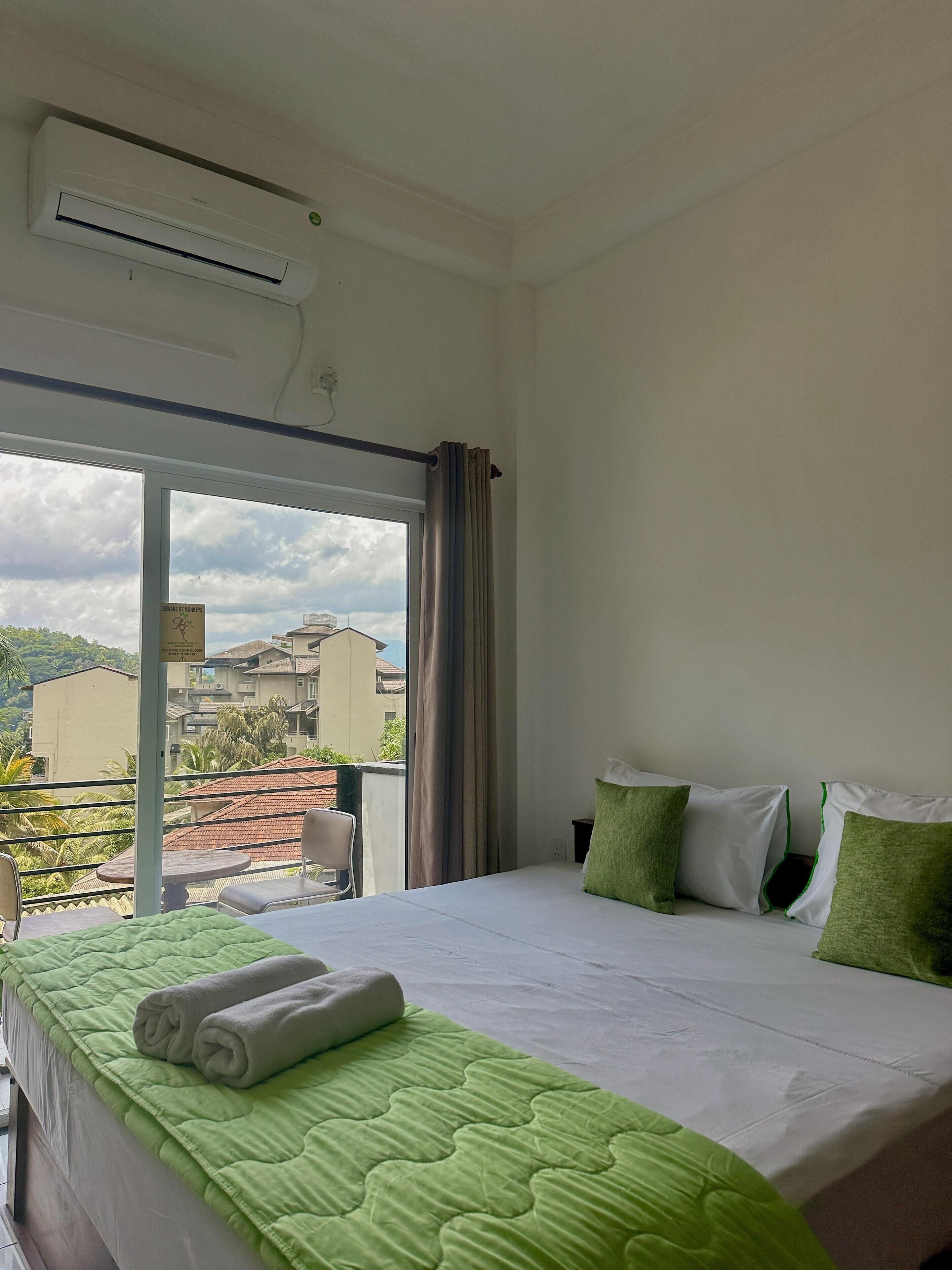 A hotel room with a bed, a green quilt, a window with curtains, and an air conditioning unit.