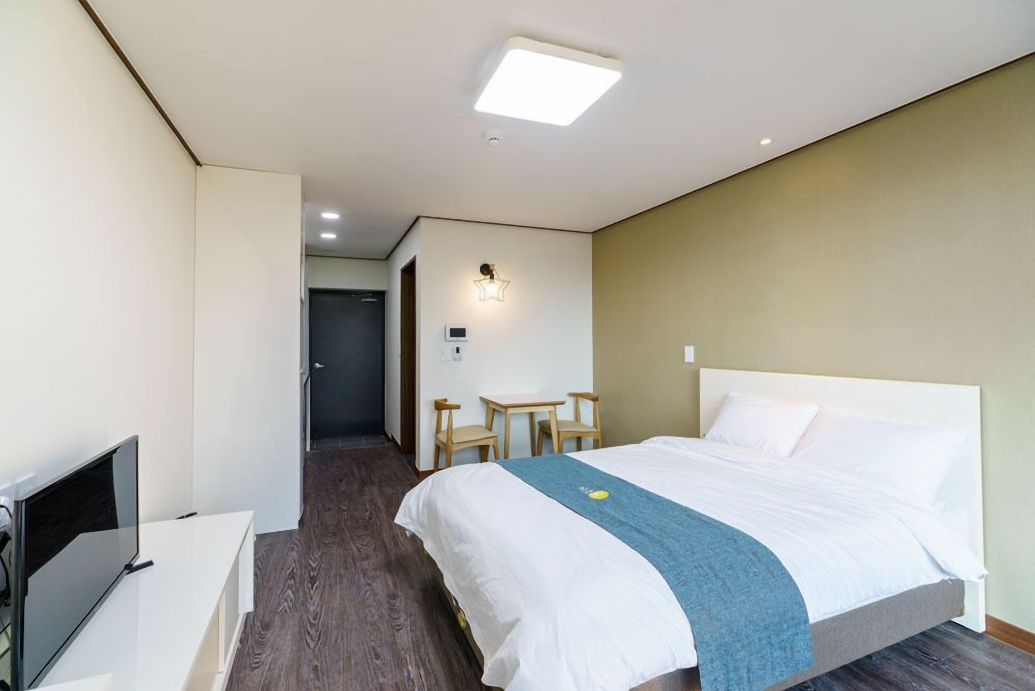 A hotel room with a bed, a desk, a TV, and a small seating area.