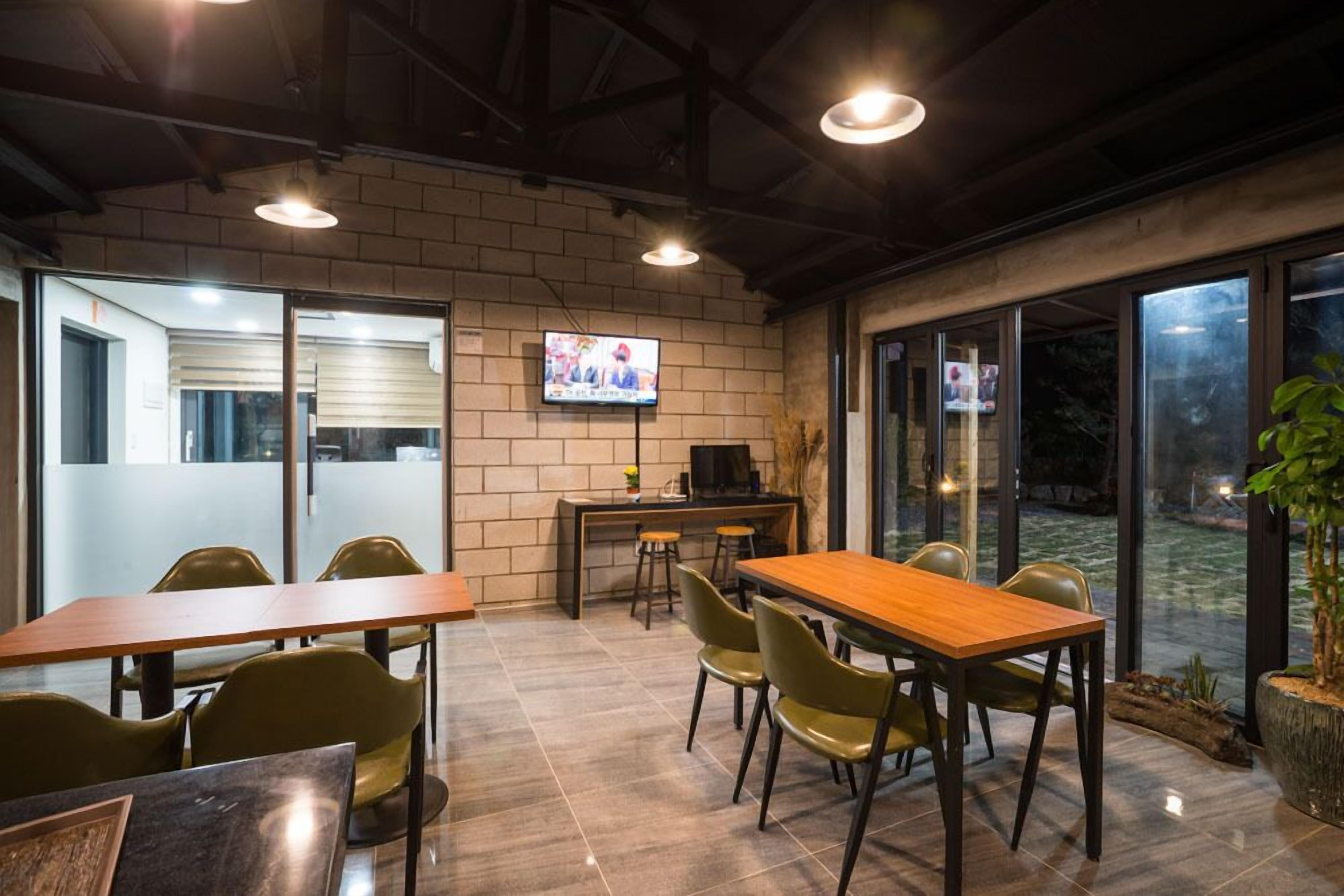 A modern conference room with a wooden table and chairs, a television on the wall, and large windows.