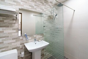 A modern bathroom with a glass shower enclosure, a white sink, and a tiled backsplash. - Misoga Pension (Seogwipo)