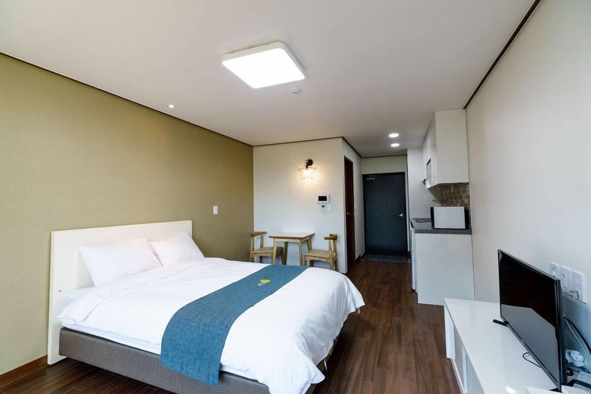 A hotel room with a bed, a desk, a TV, and a kitchenette.